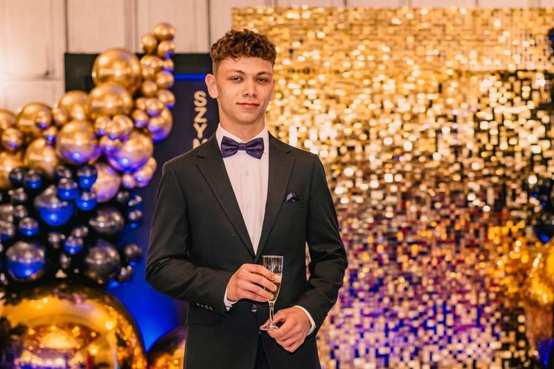 Jubilat w garniturze na tle złotej ścianki